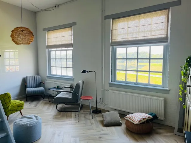 De praktijkruimte met twee grote ramen, stoelen en uitzicht over het groen
